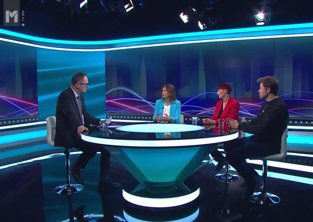 TV oddaja. Voditelj in trije gosti razpravljajo.